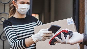 A woman in mask and gloves using her phone to make a contactless purchase